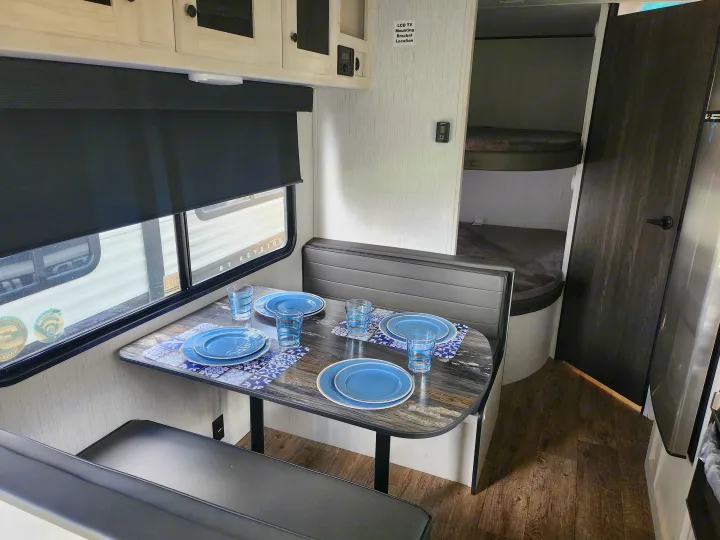 Inside an RV rental: cozy dining booth with blue dishes, adjacent to practical bunk beds, offering comfort for travelers.. Heartland RVs Trail Runner 2022