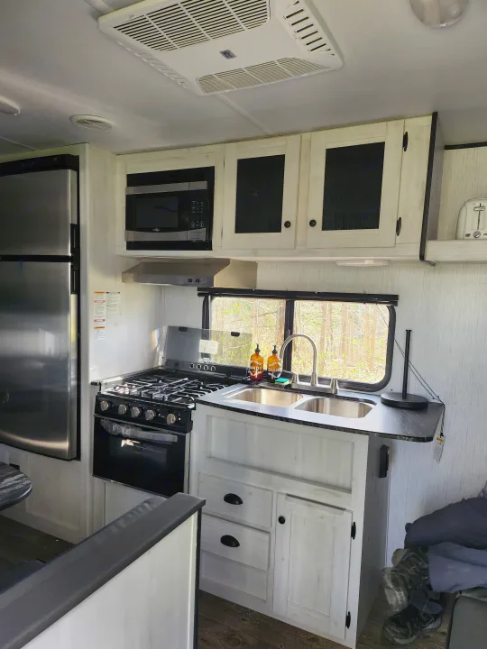Bright rv rental interior, featuring a full kitchen with stainless steel fridge, stove, microwave, sink, and light wood cabinets.. Heartland RVs Trail Runner 2022