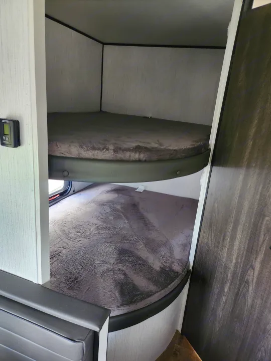 Cozy RV rental bunk beds with soft gray blankets, control panel, and window in modern RV interior.. Heartland RVs Trail Runner 2022