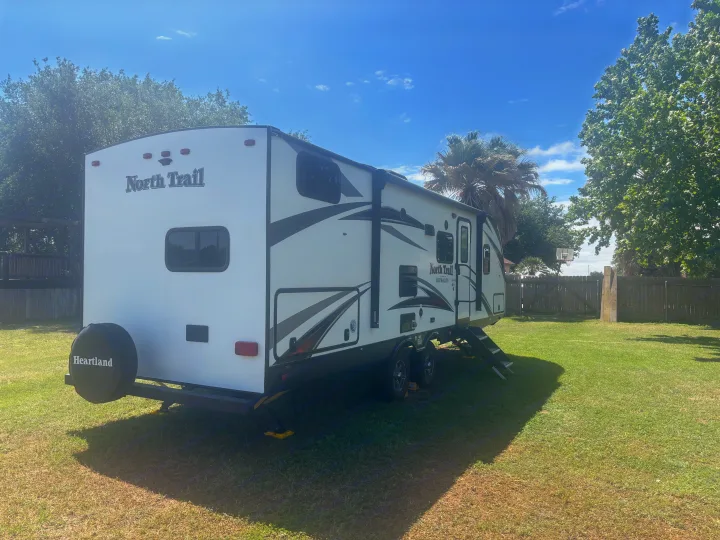 White North Trail travel trailer RV rental, ready for your next adventure. Parked on green grass with steps down.. Heartland RVs North Trail 2018