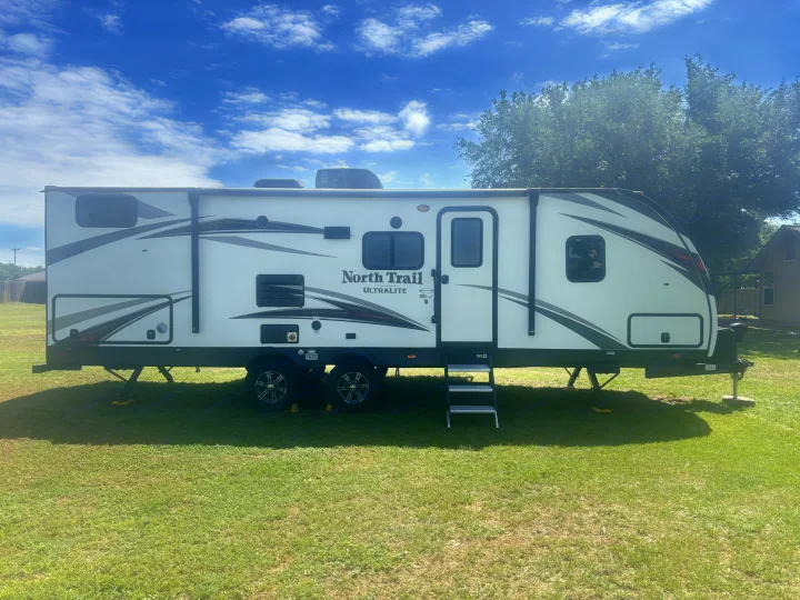 Explore with this spacious rv rental: a white North Trail Ultralite travel trailer with slide-out, parked on grass.. Heartland RVs North Trail 2018