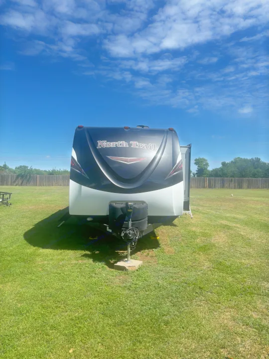 Front view of a North Trail travel trailer RV rental parked on green grass under a clear blue sky.. Heartland RVs North Trail 2018