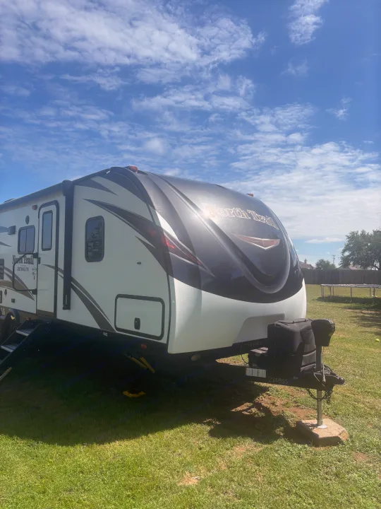 White and black travel trailer, ideal for an RV rental, parked on grass under a sunny, partly cloudy sky.. Heartland RVs North Trail 2018