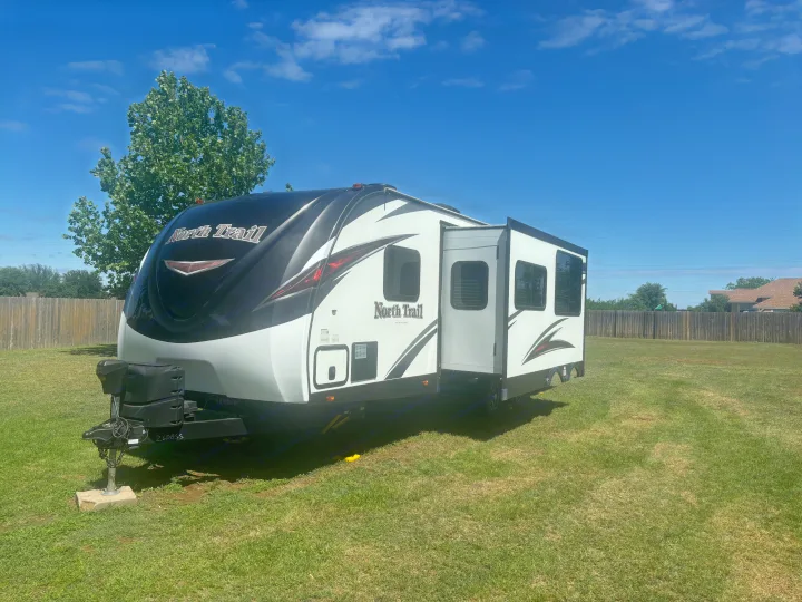 Spacious North Trail RV rental, with slide-out extended, parked on a sunny lawn under a clear blue sky.. Heartland RVs North Trail 2018