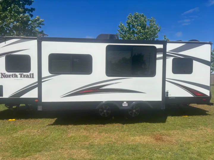 Side view of a white 'North Trail' RV rental on green grass, ready for adventure under a sunny blue sky.. Heartland RVs North Trail 2018