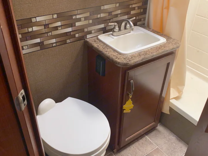 RV rental's compact bathroom with a white toilet, sink, brown vanity, and shower. Essential amenities for your travels.. Thor Motor Coach Chateau 2017