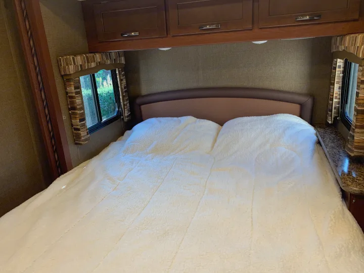Comfortable RV rental bedroom featuring a cozy white bed, padded headboard, and overhead wood cabinetry.. Thor Motor Coach Chateau 2017