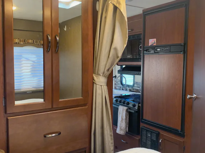 Cozy RV rental interior: kitchen with microwave, stove, sink, refrigerator, and wood cabinets. Features window blinds and a curtain.. Thor Motor Coach Chateau 2017
