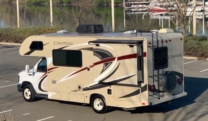 Chateau RV rental, a spacious motorhome, parked on asphalt with a scenic river and boats in the background.. Thor Motor Coach Chateau 2017