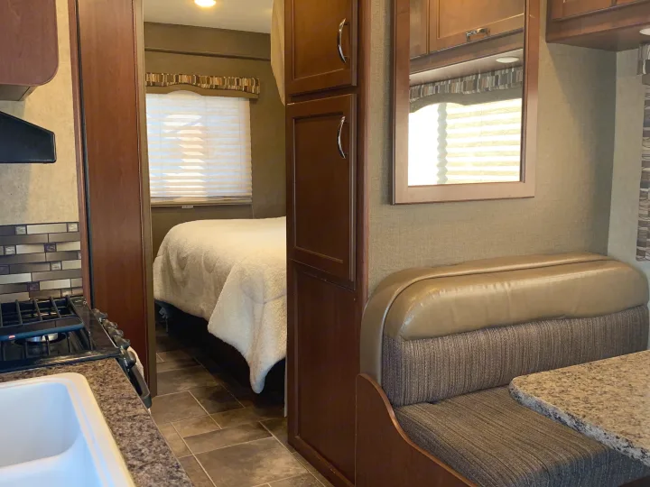 RV rental interior view: compact kitchen with sink and stove, bedroom with bed, and a dinette booth with table.. Thor Motor Coach Chateau 2017