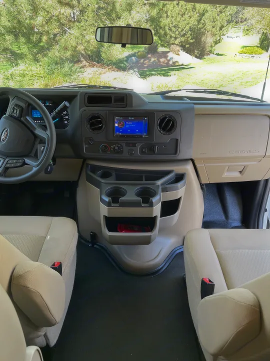 Interior view of a clean Ford E-Series RV rental cockpit, showing dashboard, steering wheel, infotainment, and seats.. Thor Coleman 2024