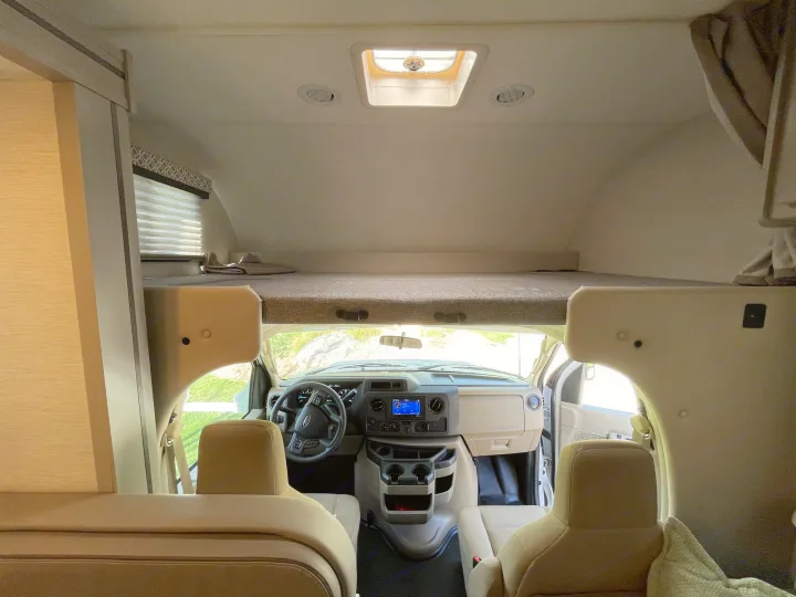 Interior of a Class C rv rental, featuring a large cab-over bunk bed and the illuminated front driver's cabin.. Thor Coleman 2024