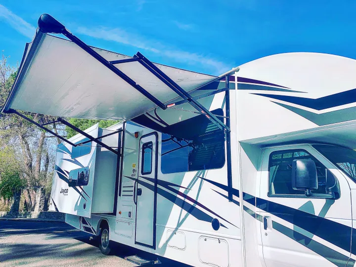 Explore with this rv rental! White Jayco RV with extended awning, parked outdoors under a blue sky, ready for adventure.. Jayco Redhawk 2019