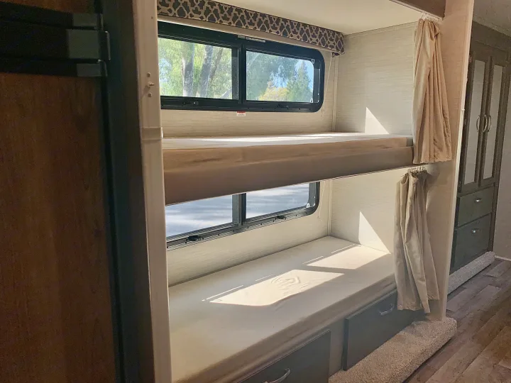 RV rental: Interior view of stacked bunk beds with windows showing trees, curtains, and built-in storage.. Jayco Redhawk 2019