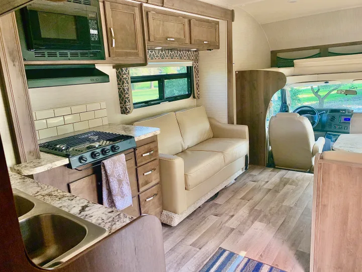 Spacious RV rental interior featuring a modern kitchen, cozy couch, and bright driver's cabin area.. Jayco Redhawk 2019