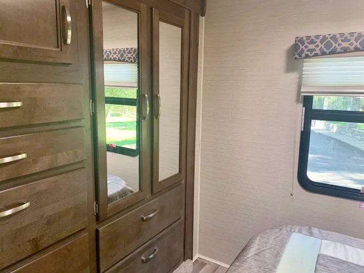 RV rental bedroom with dark wood storage, mirrored wardrobe doors, and a window with outdoor views.. Jayco Redhawk 2019
