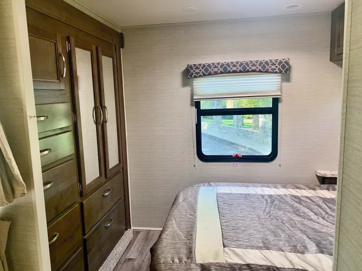 Spacious RV rental bedroom with a comfy bed, large window, and built-in wardrobe/drawers, offering practical storage for your travels.. Jayco Redhawk 2019