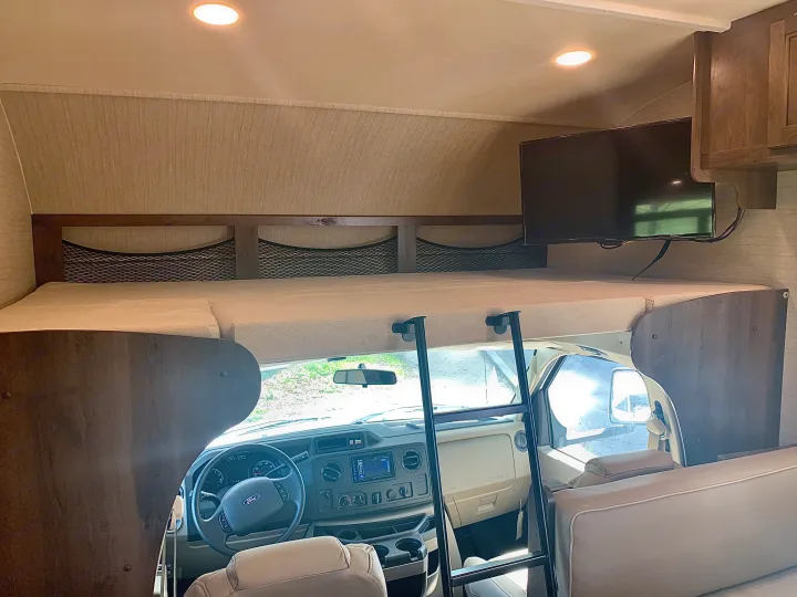 RV rental interior: cozy cab-over bunk with TV, access ladder, and a full view of the front cockpit. Ready for adventure.. Jayco Redhawk 2019