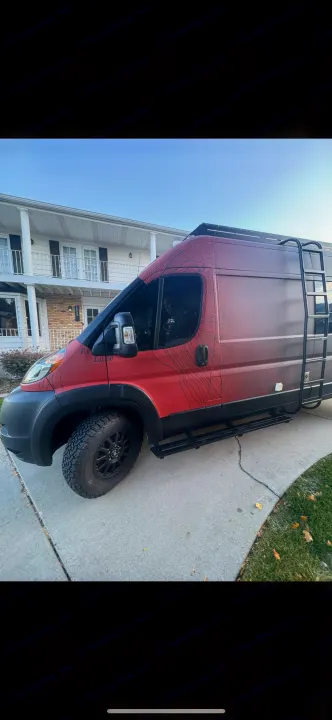 Customized red RV rental parked on a driveway, featuring rugged tires, side steps, and a roof ladder for adventure.. Dodge RAM Dodge RAM Promaster 2500 2021