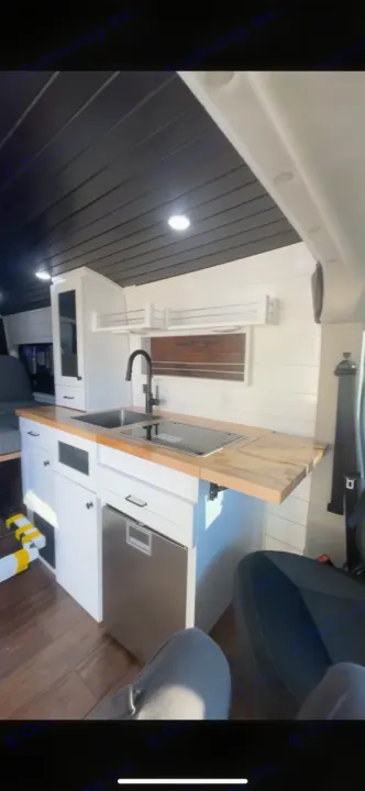 Modern RV rental kitchen with a black sink, induction cooktop, and stainless steel fridge set in a bright interior.. Dodge RAM Dodge RAM Promaster 2500 2021