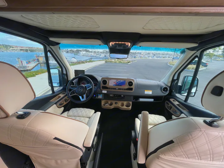 Luxury RV rental interior: Cream quilted seats, Mercedes-Benz cockpit, & a stunning marina view outside.. Mercedes-Benz Sprinter 2023