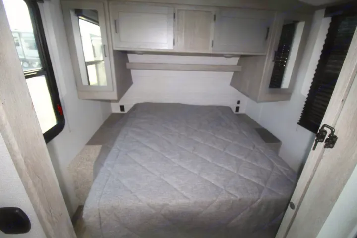 This RV rental bedroom features a comfy queen bed with overhead storage and windows, offering a cozy space for travel.. Keystone RV Outback Ultra-Lite 2020