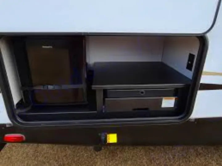 Enjoy an RV rental with an outdoor kitchen: an open compartment revealing a mini-fridge and slide-out grill/cooktop unit.. Keystone RV Outback Ultra-Lite 2020