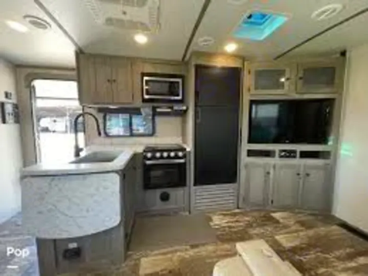 This RV rental interior shows a modern travel trailer kitchen with gray cabinets, appliances, and an entertainment center in the living area.. Keystone RV Outback Ultra-Lite 2020