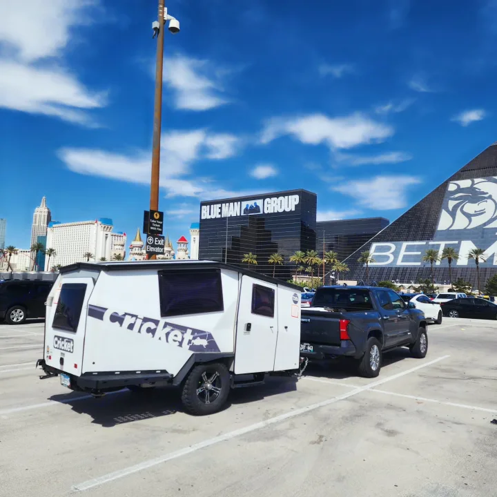 An rv rental Cricket camper towed by a truck, parked in Las Vegas with the Luxor and Excalibur hotels in the background.. TAXA TAXA Trailer 2021