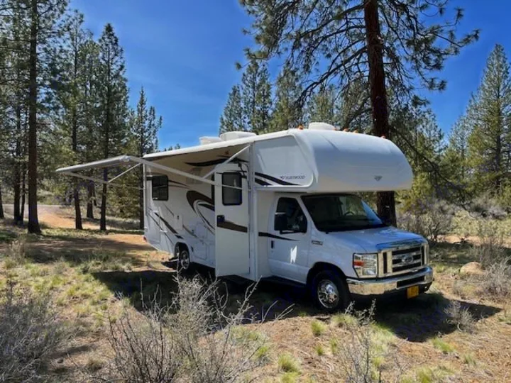 RV rental parked in a sunny wooded area with awning extended. Perfect for camping adventures.. Jamboree Searcher 2013