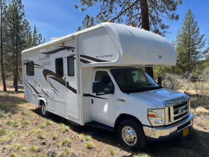White Class C Fleetwood RV rental, parked under a clear sky among pine trees. Perfect for your outdoor adventure!. Jamboree Searcher 2013