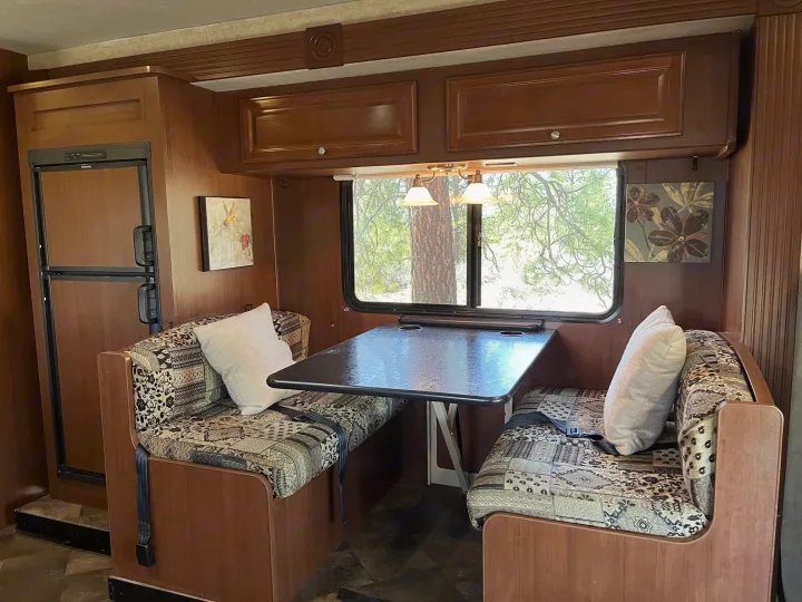 Cozy RV rental dinette featuring cushioned booth seating, a functional table, and a refrigerator to the left.. Jamboree Searcher 2013
