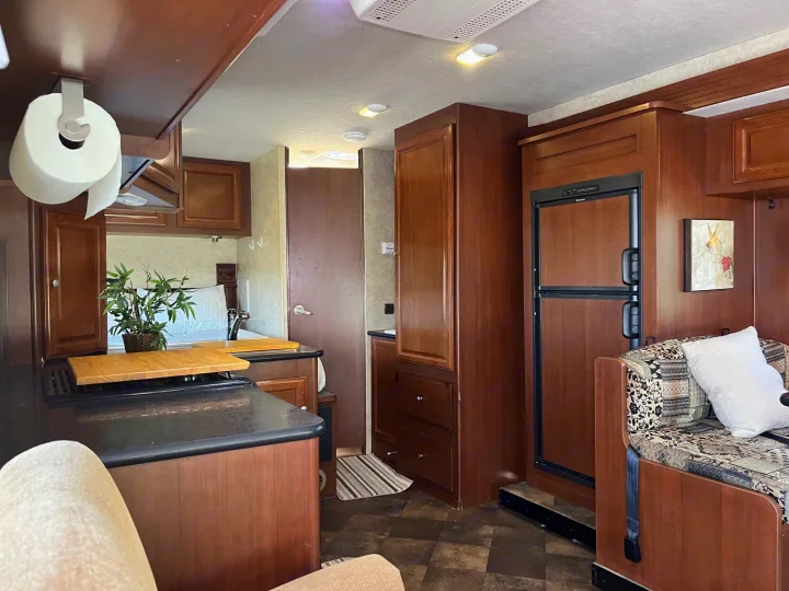 RV rental interior: Features a compact kitchen, dinette seating, and wood cabinetry, offering a functional living space for travel.. Jamboree Searcher 2013