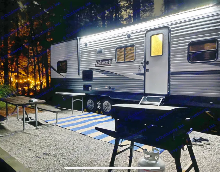 A brightly lit RV rental at a night campsite, featuring a grill, picnic table, and outdoor string lights.. Coleman 262BH 2021