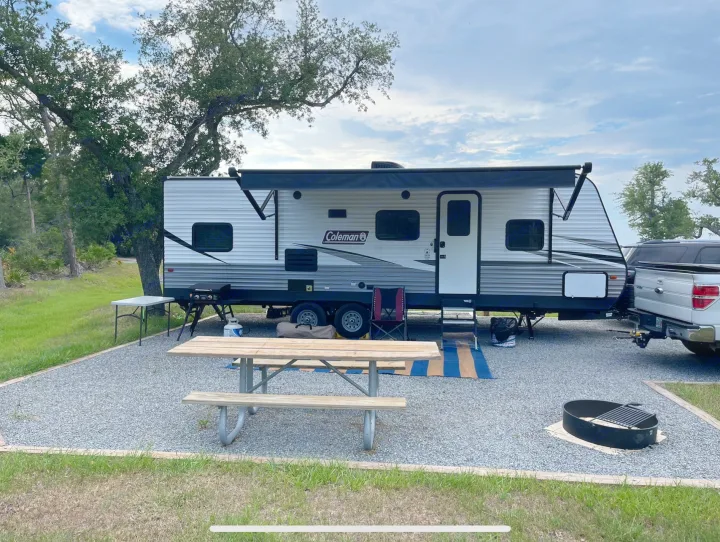 Scenic RV rental campsite with a Coleman travel trailer, picnic table, grill, and fire pit, ready for adventure.. Coleman 262BH 2021