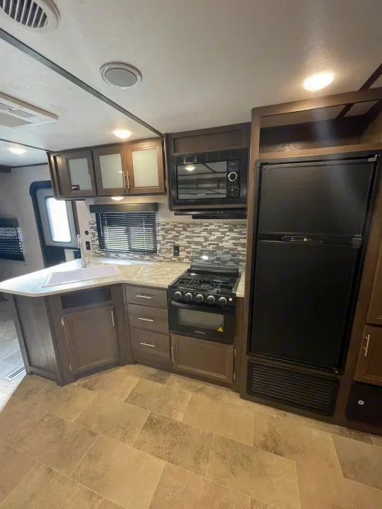 RV rental kitchen with modern dark wood cabinets, sink, microwave, gas range, and large refrigerator.. Coleman 262BH 2021