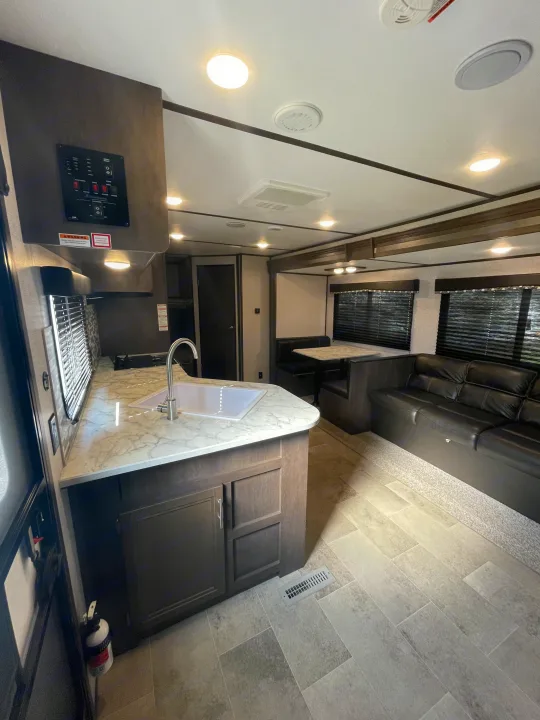 Spacious RV rental interior featuring a modern kitchen with a sink, dining booth, and a comfortable sofa living area.. Coleman 262BH 2021