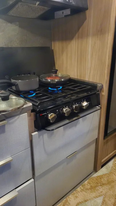 Inside an RV rental: a kitchen area with a gas stove actively cooking food in two pots.. Winnebago Minnie Winnie 2021