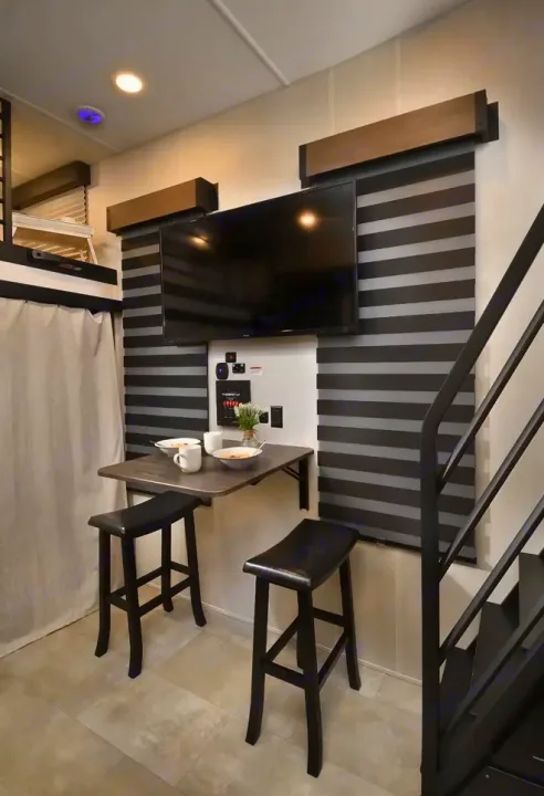 This RV rental offers a compact dining area: wall-mounted table, two stools, and TV. Modern design with striped blinds.. Forest River Timberwolf 16ML 2024