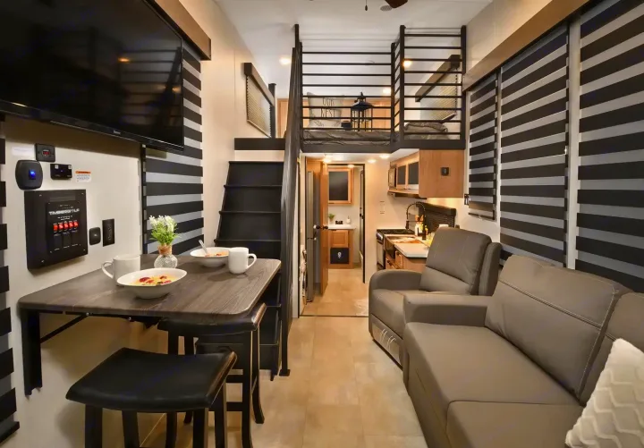 This RV rental's modern interior has a living room, full kitchen, dining, and a cozy loft bedroom with stairs.. Forest River Timberwolf 16ML 2024