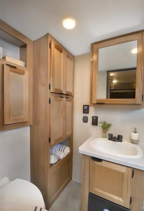 Compact RV rental bathroom with light wood cabinets, sink, mirror, and toilet, offering practical storage.. Forest River Timberwolf 16ML 2024