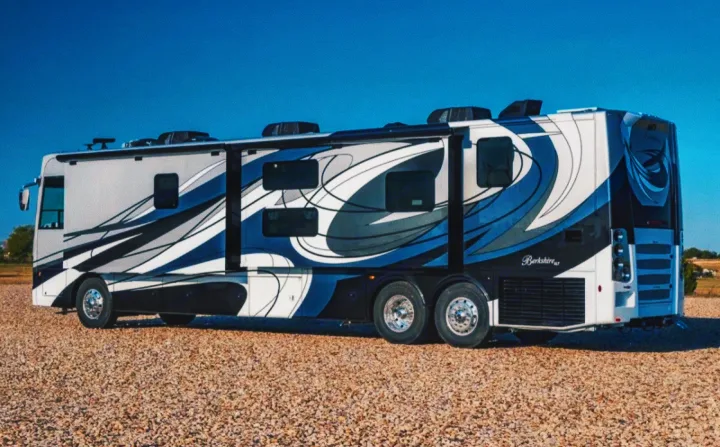 A stylish, large RV with blue, black, and white swirl graphics is parked on gravel under a clear sky. Ideal for rv rental road trips.. Forest River Berkshire 2023