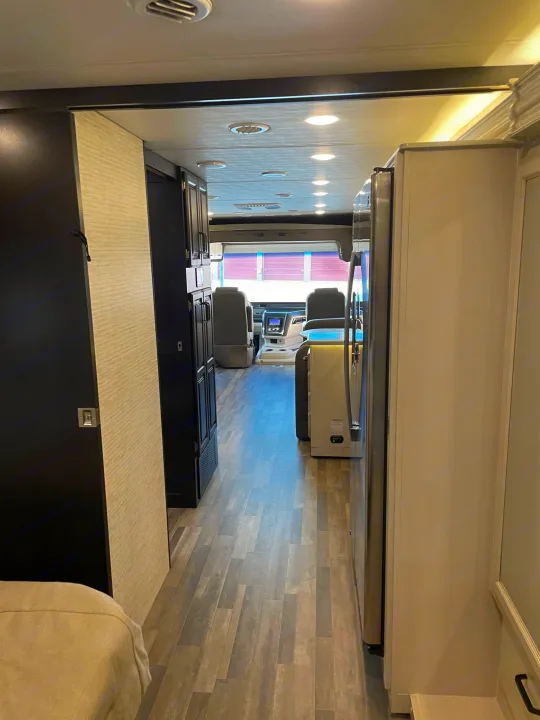 Spacious RV rental interior featuring a hallway with wood-look flooring leading to the cockpit, kitchen area, and bright lighting.. Entegra Coach Vision XL 2024
