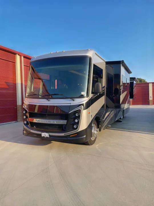 Sleek RV rental motorhome, parked with slides extended by red storage units under a blue sky.. Entegra Coach Vision XL 2024