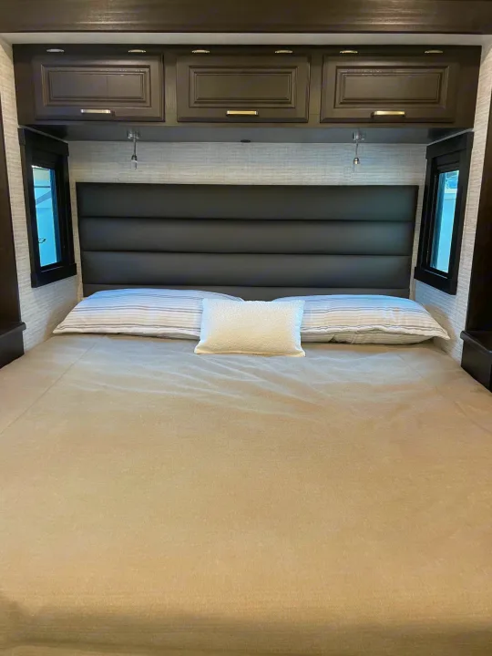 RV rental bedroom: Comfortable bed, dark overhead storage, side windows, and reading lights in compact space.. Entegra Coach Vision XL 2024