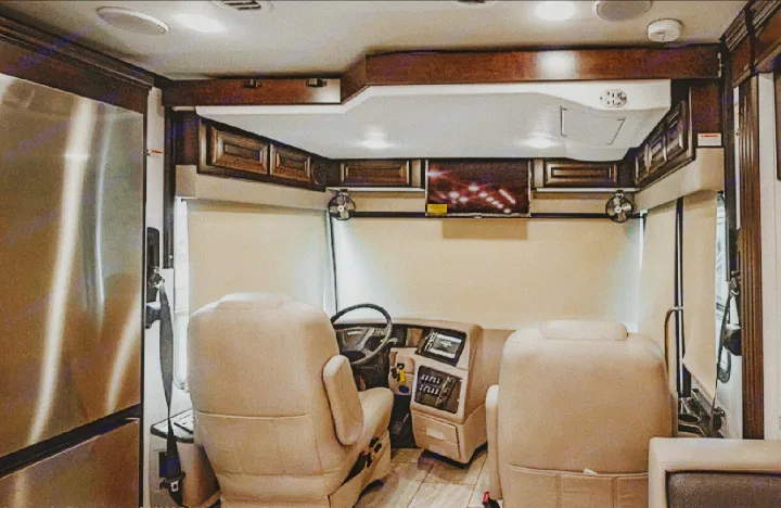 Front interior of an RV rental: comfortable driver and passenger seats, dashboard, TV, and a large stainless steel fridge.. Forest River Berkshire 2023