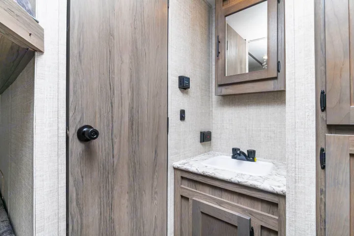Functional RV rental bathroom vanity with sink, medicine cabinet, and wood-grain storage. A closed door is to the left.. Gulf Stream Friendship 2022