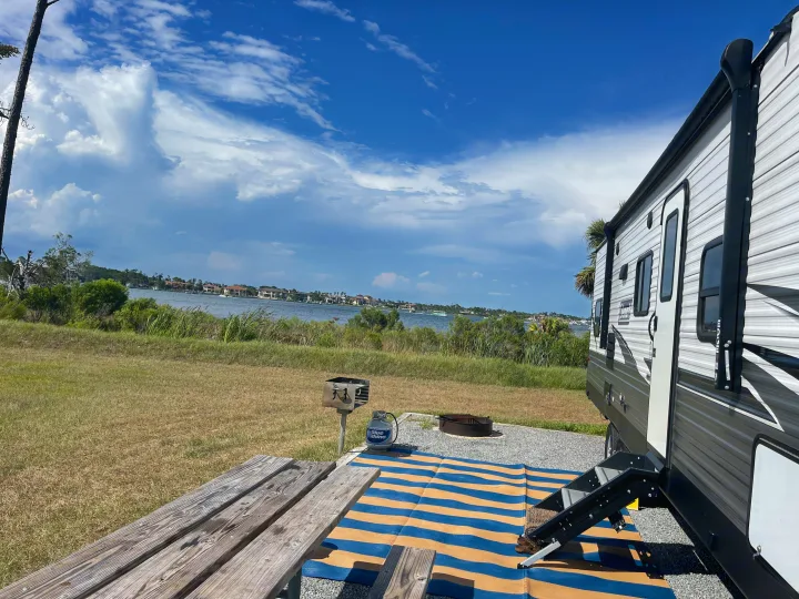 Scenic rv rental at a waterfront campsite with a picnic table, grill, and view of houses across the water.. Coleman 262BH 2021