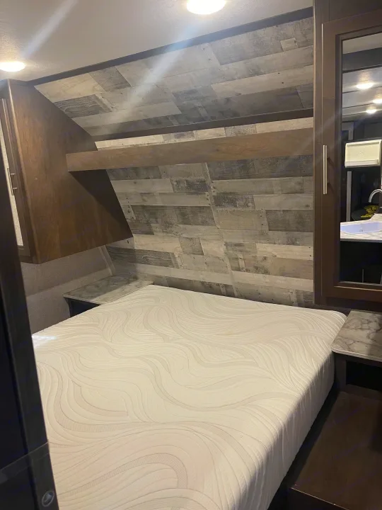 Experience comfort in this RV rental bedroom: a large bed, stylish wood paneling, and a mirrored closet reflecting a sink vanity.. Coleman 262BH 2021
