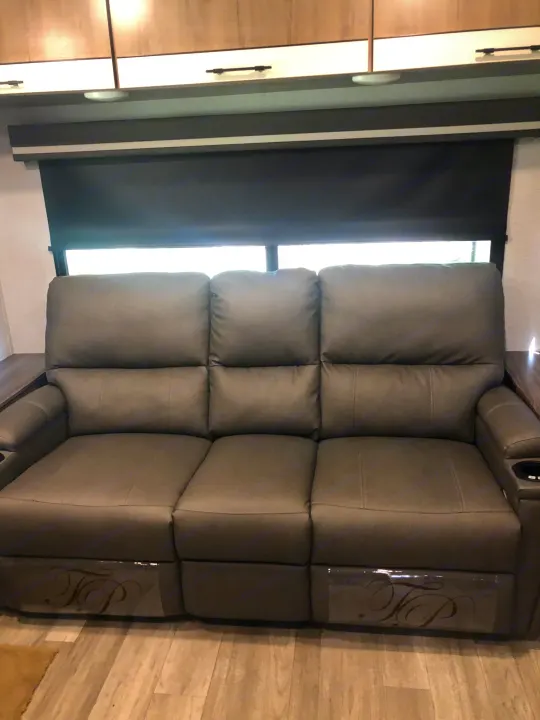 RV rental interior features a cozy three-seat reclining sofa with cup holders, perfect for relaxing after a long day of travel.. Grand Design Imagine 2023